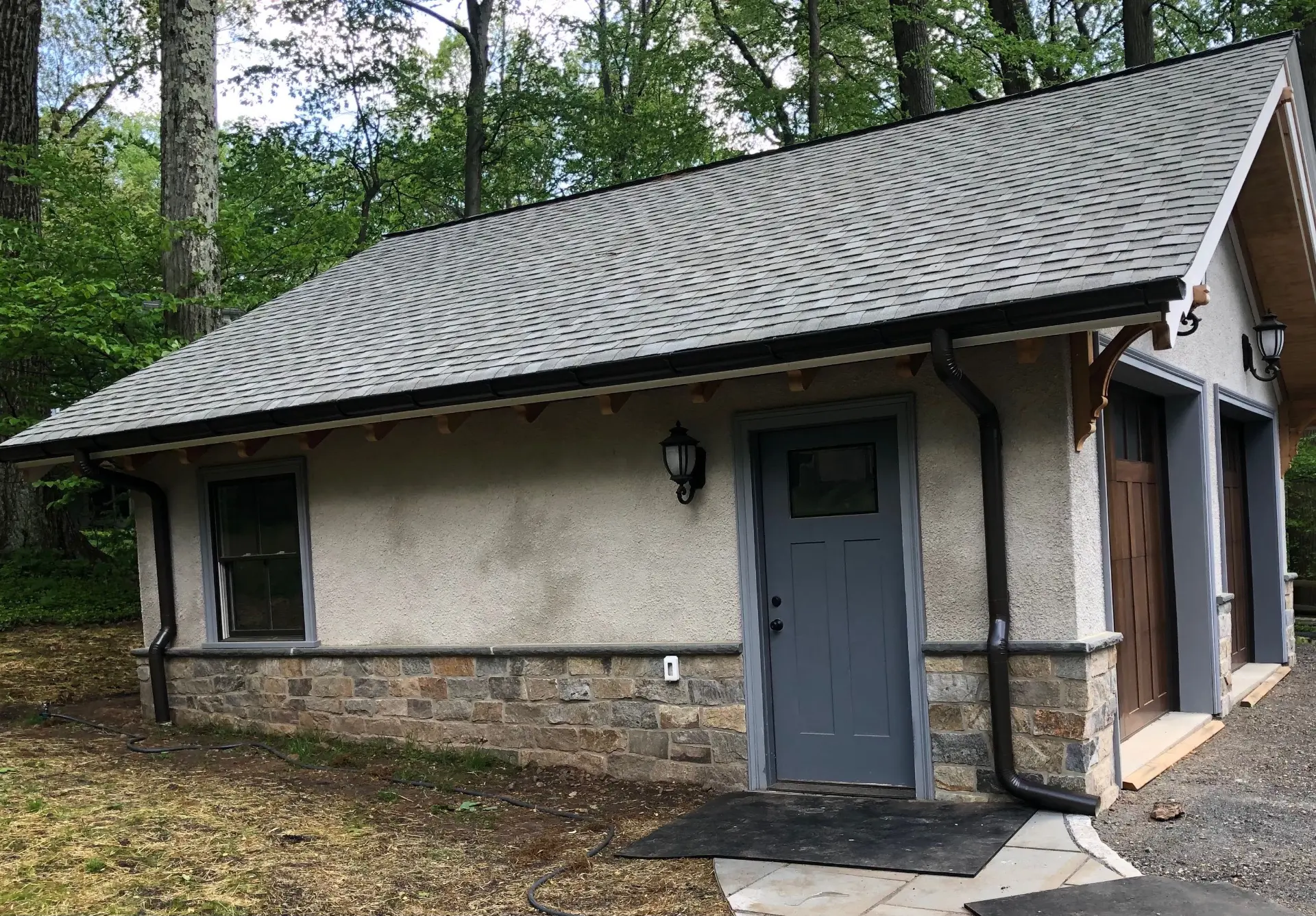 Stone and stucco garage with new dark gutters and two downspouts