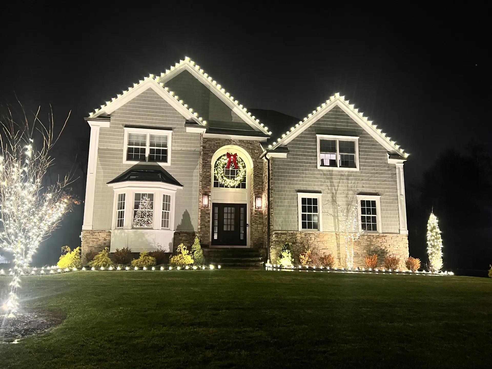 Home outlined in warm white holiday roofline lights at night