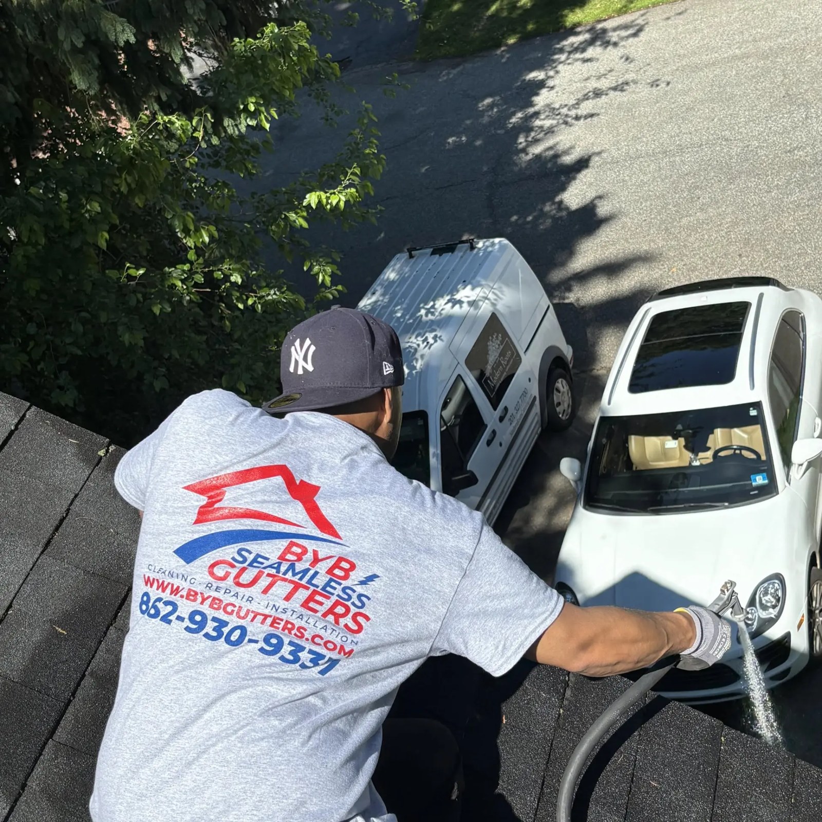BYB Gutters technician on a roof rinsing a gutter with a hose